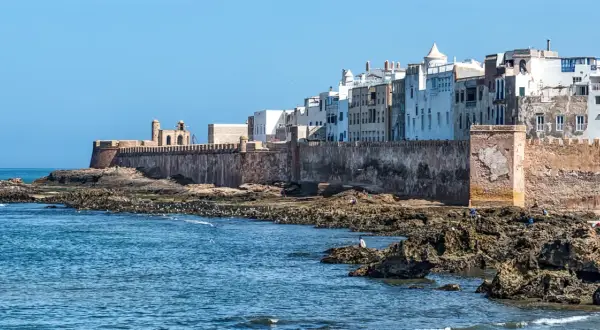 Vue des remparts d'Essaouira, avec des maisons blanches en arrière-plan. Les rochers et la mer invitent à toutes les activités.