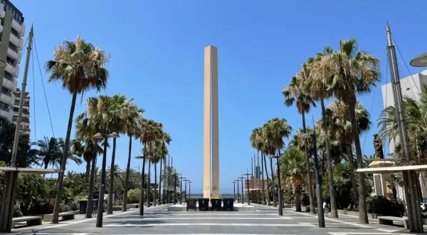 Un obelisco se alza en la plaza de las velas Almería, flanqueado por palmeras y un cielo azul despejado.