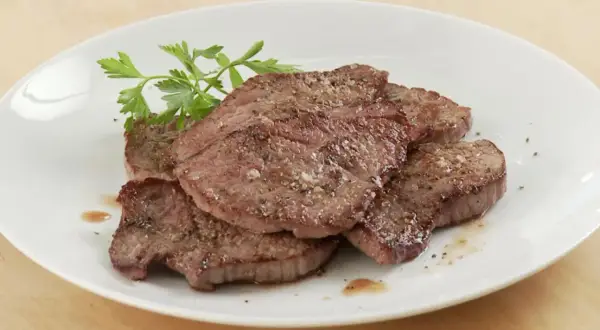 Saftiges Schnitzel Natur, gewürzt mit Pfeffer und Salz, auf einem weißen Teller mit Petersilie garniert.