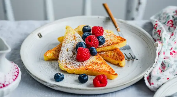 Goldbraune French Toast-Scheiben, bestäubt mit Puderzucker und garniert mit frischen Beeren. Ein perfektes Frühstück, das Lust auf mehr macht.