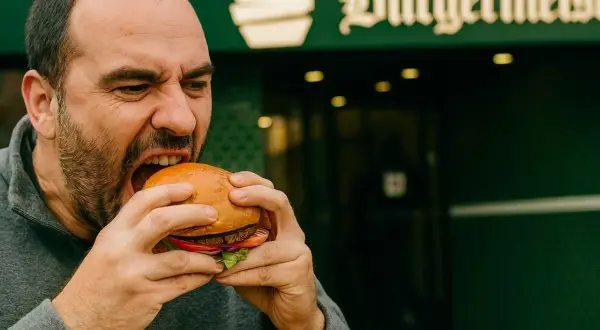 Mężczyzna z pasją wgryza się w soczystego burgera, zastanawiając się, skąd pochodzą hamburgery.