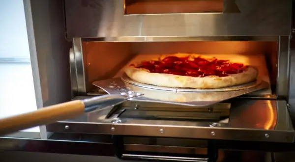 Pizza z pepperoni na łopacie wkładana do pieca.