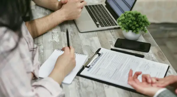 Osoby przy stole analizują dokument "Home Insurance Policy". Kobieta notuje, mężczyzna patrzy na laptopa. Może to być związane z wefox wypowiedzenie oc.