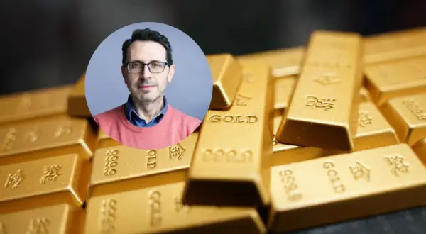 Mężczyzna w okularach na tle sztabek złota. Czy złoto traci na wartości? Analiza eksperta.