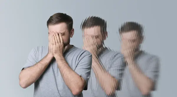 Mężczyzna z rękami na twarzy, doświadczający wizualnych zaburzeń, jak przy delirium tremens.