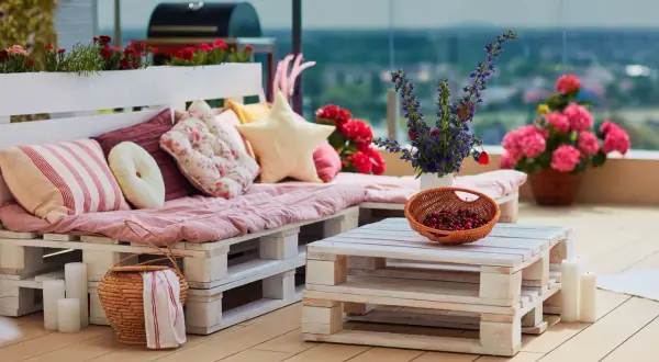 Divano e tavolino da caffè creati con il riciclo pallet, decorati con cuscini colorati, fiori e una cesta di ciliegie.