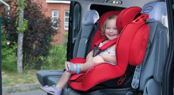 Ein lächelndes Kind sitzt sicher in einem roten Kindersitz im Auto. Perfekt für den nächsten Ausflug oder als Taxi Kindersitz.