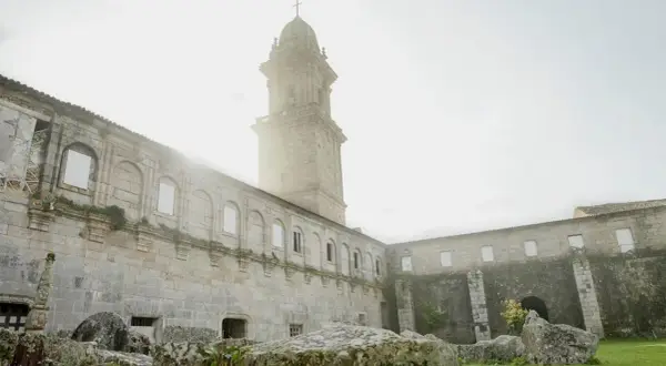 El imponente **monasterio de Oia** se alza bajo un cielo brumoso, con su torre campanario y sus muros de piedra evocando historias de siglos pasados.