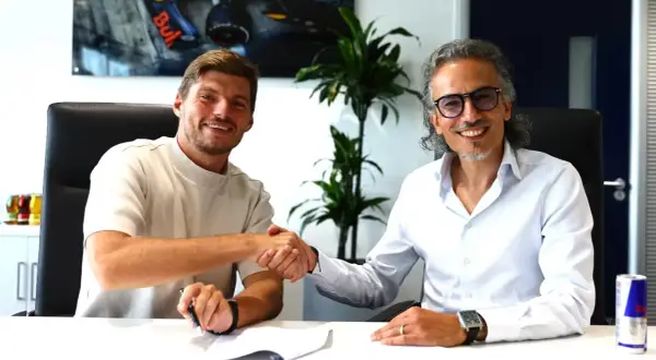 Max Verstappen sonríe mientras estrecha la mano de un hombre con gafas, sellando un acuerdo.