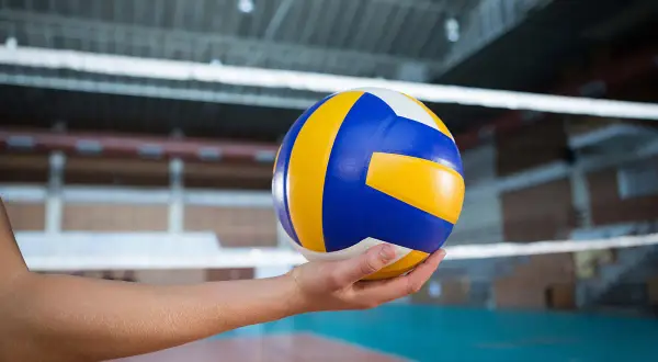 Piłka do siatkówki w dłoni, gotowa do zagrania nad siatką w hali sportowej.