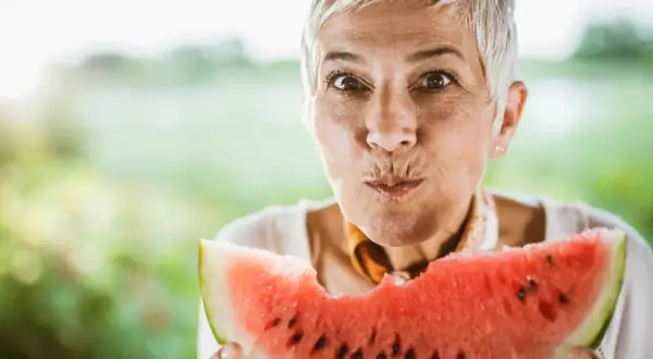 Glad kvinna med grått hår njuter av en saftig vattenmelon. Perfekt för ett uppfriskande vattenmelon recept.