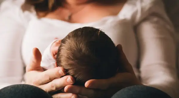 Dłoń matki trzymająca główkę noworodka.