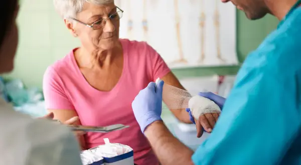 Arzt verbindet die Hand einer älteren Frau. Die Szene zeigt die wundversorgung nach op zu hause.