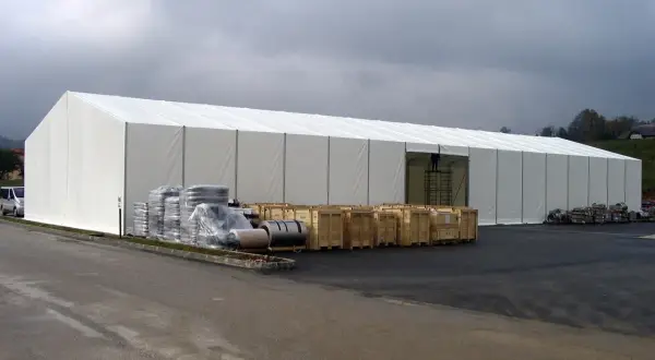 Ampia tensostruttura bianca, con merci stoccate all'esterno. Ottenere i permessi per queste strutture è fondamentale per la logistica.