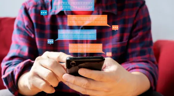Mężczyzna trzyma smartfon, a nad nim pojawiają się dymki czatu. Dowiedz się, jak zaktualizować Messengera na telefonie, aby zawsze być na bieżąco.