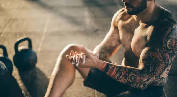 Mann mit beeindruckendem Tattoo am Oberarm bereitet sich mit Magnesium vor. Kettlebells im Hintergrund.