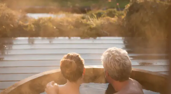 Pareja disfrutando de una relajante experiencia en un jacuzzi al atardecer. El vapor se eleva mientras se abrazan, creando un momento íntimo.