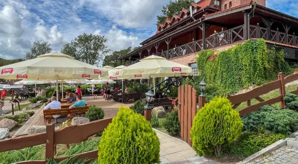 Odkryj najlepsze restauracje na Mazurach! Letni ogródek z widokiem na jezioro, gdzie można delektować się posiłkiem pod parasolami.
