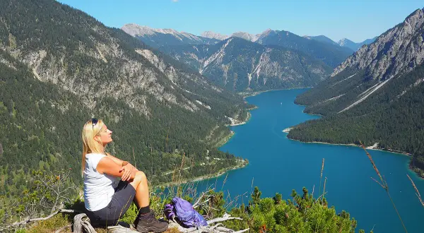 Frau genießt Ausblick beim Plansee Wandern. Türkiser See, grüne Berge und blauer Himmel.