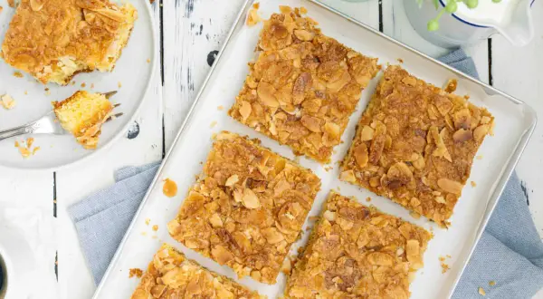 Saftiger butterkuchen ohne hefe, bestreut mit knusprigen Mandelblättchen. Ein Stück auf einem Teller mit einer Gabel.