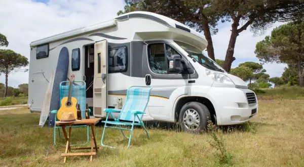En vit husbil, en personbil klass 2, står parkerad i gräset. Surfbrädor, en gitarr och campingstolar antyder en avkopplande semester.