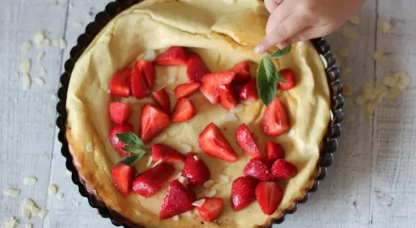 Puszysty dutch baby z truskawkami i płatkami migdałów, dekorowany przez dziecko.