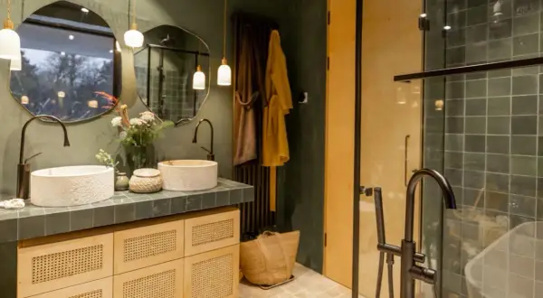 Bagno stile boho chic con doppio lavabo in pietra, mobili in legno e vimini, specchi irregolari e doccia con piastrelle verdi.
