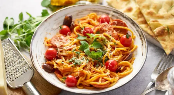 Pyszny makaron z chorizo, pomidorkami koktajlowymi i świeżą bazylią, posypany parmezanem. Idealny na szybki obiad.