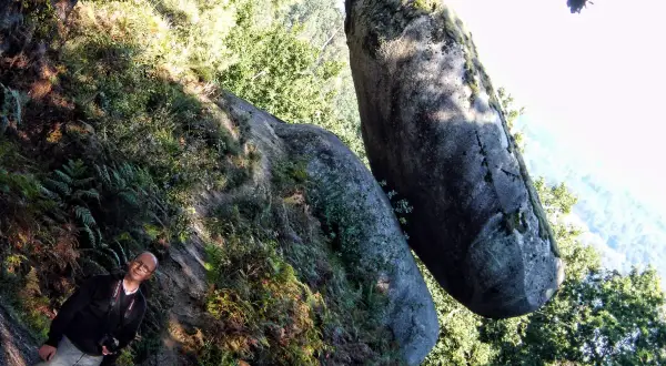 Hombre sonriente junto a una roca suspendida, un ejemplo de la pena do equilibrio en la naturaleza.