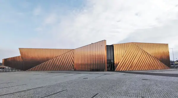 Nowoczesny budynek muzeum ognia z miedzianą elewacją, przypominającą płomienie.