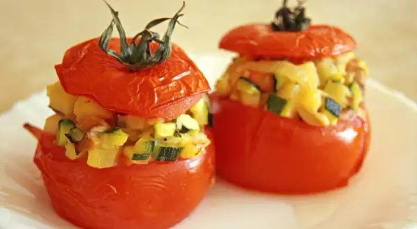 Deux tomates farcies, garnies d'un mélange de légumes et de fromage, sont présentées sur une assiette blanche.