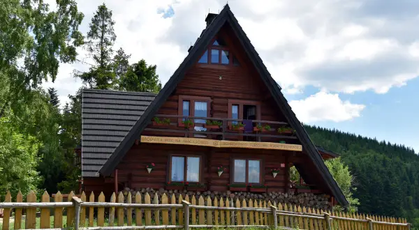 Drewniana bacówka PTTK na Maciejowej, schronisko turystyczne z Rabki, otoczone zielenią i drewnianym płotem.