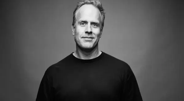 Porträtt av Magnus Lindqvist, en man med gråsprängt hår och ett vänligt leende, klädd i en svart t-shirt.