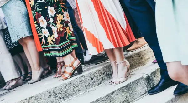 Gäste in festlicher Kleidung, die den **Dresscode Hochzeit** erfüllen, stehen auf einer Steintreppe. Bunte Kleider und elegante Schuhe.