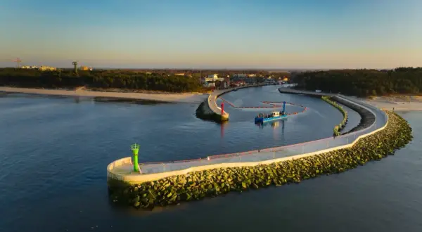 Port w Mrzeżynie z falochronami i latarniami morskimi. Widoczna łódź pogłębiarka. To jedne z mrzeżyno atrakcje.