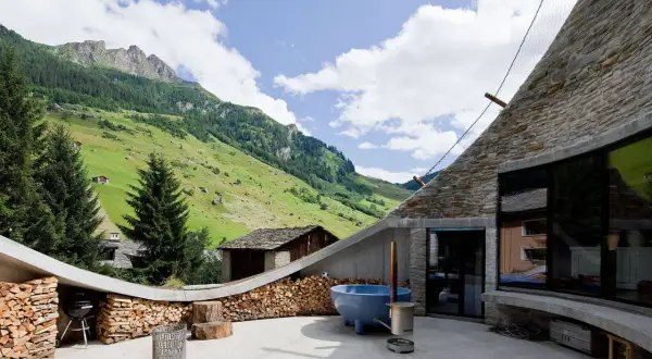 Dekorativ gestapeltes Brennholz umrahmt den Grill und die Terrasse mit Bergblick. Ein blaues Becken und ein Feuerkorb laden zum Entspannen ein.