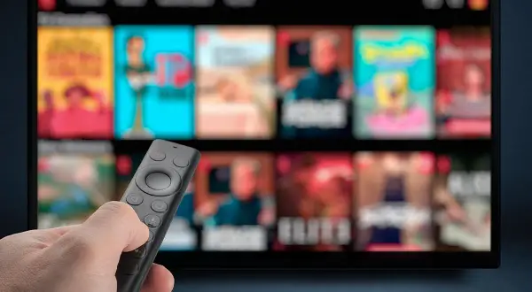 Dłoń trzymająca pilot do telewizora, ekran wyświetla menu z filmami. Dowiedz się, jak wyłączyć napisy w telewizorze.