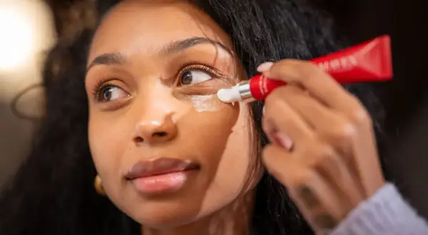 Donna applica crema contorno occhi per contrastare i segni sotto gli occhi, con un tubetto rosso.