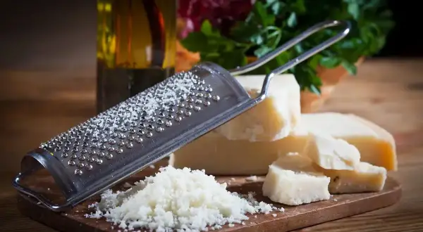 Tarka z grudkami sera, obok kawałki Grana Padano i parmezanu, gotowe do starcia.