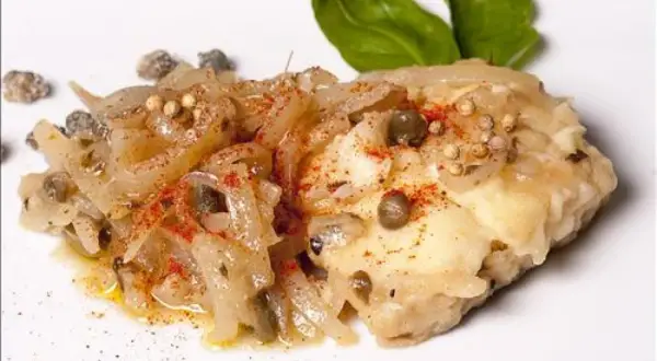 Un morceau de lotte poisson, cuisiné avec des oignons, des câpres et des épices, garni de feuilles de basilic.