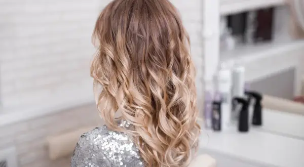 Fryzura z efektem ombre blond, falowane włosy w połyskującej, srebrnej bluzce.