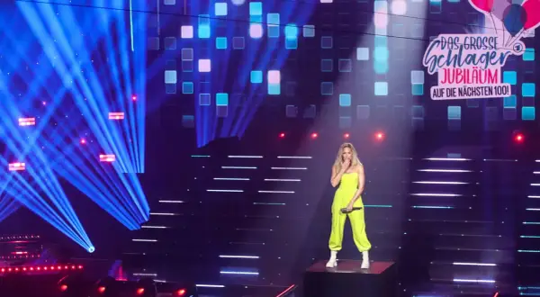Eine Sängerin steht auf einer Bühne, umgeben von blauen Lichtstrahlen und einem LED-Bildschirm, der "Das große Schlager-Jubiläum" zeigt. Sie ist eine der vielen Schlagerstars Deutschlands.