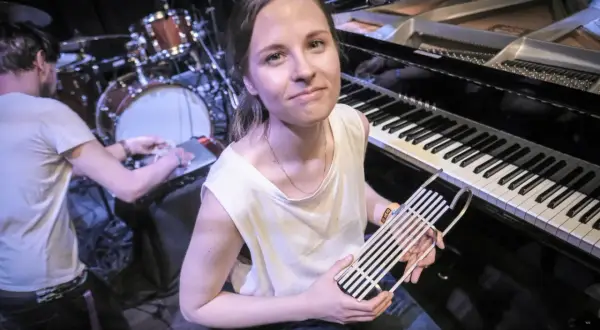 Hania Rani, przy fortepianie, trzymając w dłoniach nietypowy instrument, gotowa do tworzenia swoich unikalnych utworów.