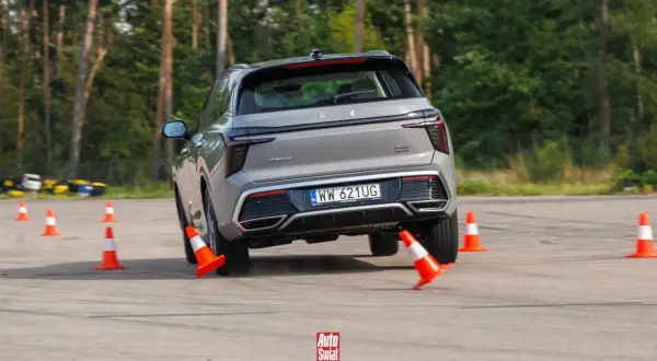 Szary SUV wykonuje test łosia, gwałtownie skręcając między pomarańczowymi pachołkami na torze.