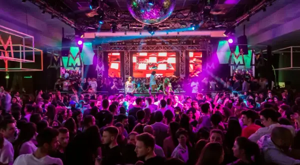 En stor publik njuter av 30 års fest aktiviteter med DJ och discokula. Ljusshow i lila och rosa skapar en festlig stämning.