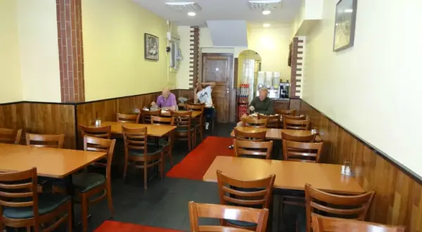 Interiör av en turkisk restaurang i Stockholm. Flera bord med trästolar och röda mattor. Tre gäster sitter vid borden.