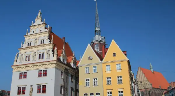 Kolorowe kamienice i wieża kościelna na rynku w Nysie pod błękitnym niebem.
