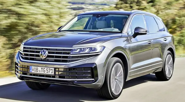 Szary Volkswagen Touareg pędzi po drodze, otoczony zielenią.