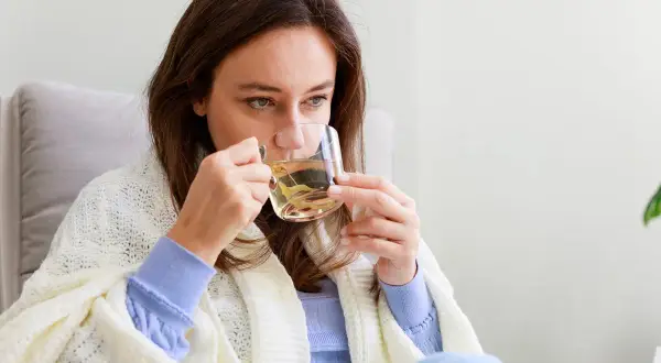 Kobieta pije napar z ziół, który może pomóc na biegunkę. Otulona kocem, szuka ulgi w domowym zaciszu.