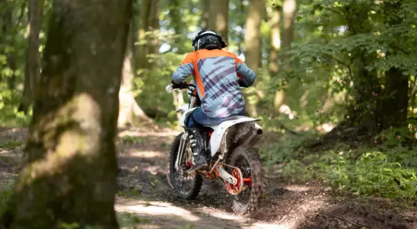 Motocyklista w kasku i kolorowej bluzie pędzi po leśnym torze. Zastanawiasz się, prawo jazdy na crossa od ilu lat jest potrzebne, by poczuć taką wolność?